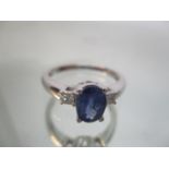 An 18ct white gold ring set with an oval blue sapphire, approximately 1.25ct, flanked by two
