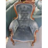 A Victorian walnut armchair having blue button back upholstery, with scrolled arms and castors