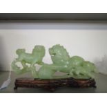 A Chinese green jade carved group of three lion dogs 10 7/8" long, mounted on a wooden base