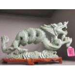 A Chinese carved model of a dragon in light green soapstone mounted on a wooden stand
