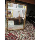 A rectangular gilt framed wall mirror with leaf decorated gilt frame