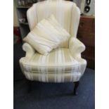 A good quality wing back armchair in a cream striped material with two scatter cushions on