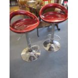 A pair of modern adjustable chrome bar stools with foot rests and metallic red seats