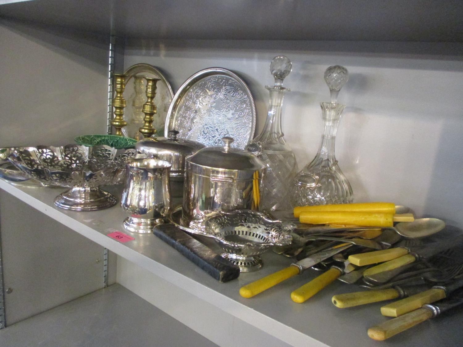 A mixed lot to include two cut glass decanters, silver plated trays, brass candlesticks, cutlery and