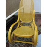 A modern light wood, cane seated rocking chair with two mixed cushions