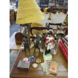 A brass column style table lamp with a modern mustard coloured shade, two bronzed tribal figures and