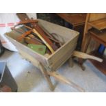 A vintage wheelbarrow containing mixed tools, walking sticks and other items