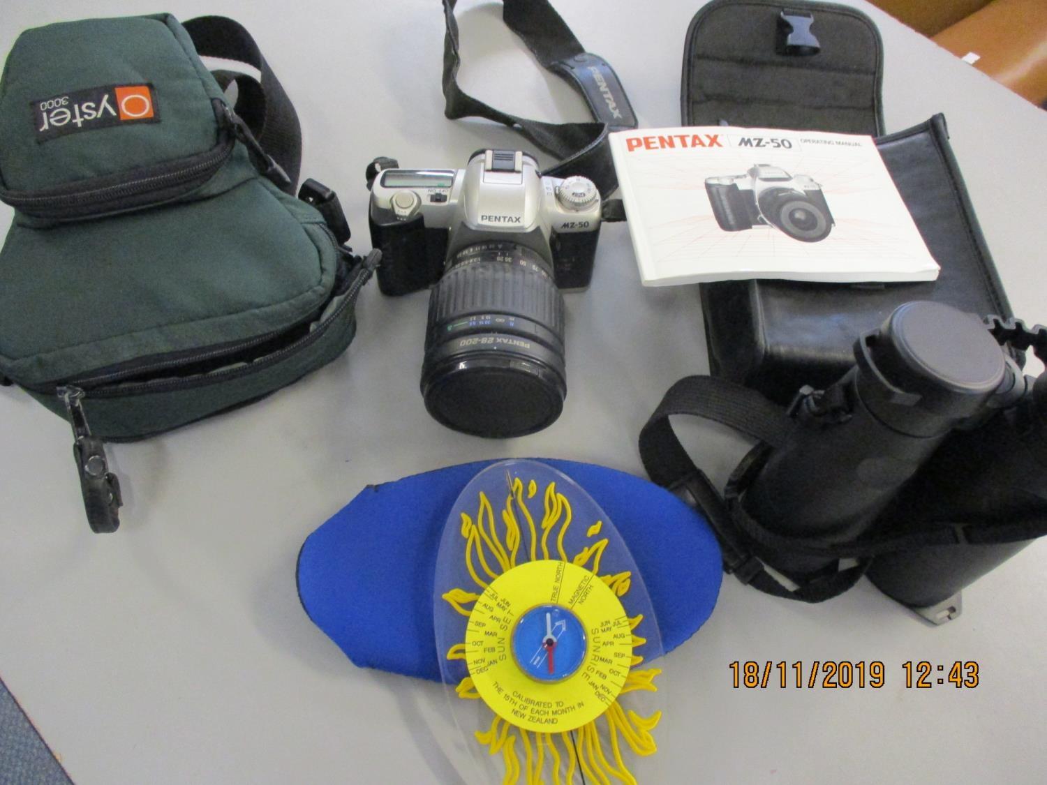 A Pentax MZ50 camera and travel case, modern Minox binoculars and a New Zealand sun dial