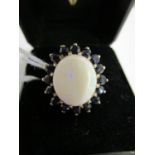 A 9ct gold opal and sapphire cluster ring, the large round opal surrounded by sixteen sapphires, 5.