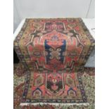 A Middle Eastern hand woven rug, geometrical designs on a red ground and tasselled ends, 78" x 39