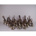 A set of nineteen Hand Bells, one marked Mears, with tooled leather straps, each marked on the