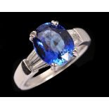 A Sapphire and Diamond Ring claw-set oval-cut sapphire, 4.06cts,between two pairs of tapered diamond