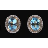 A pair of Blue Topaz and Diamond Cluster Earrings each claw-set oval cabochon topaz within a frame