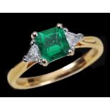 An Emerald and Diamond Ring claw-set step-cut emerald, 0.76cts, between two triangular-cut