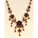 A Garnet Fringe Necklace, the front with three graduated flowerhead plaques set round stones with