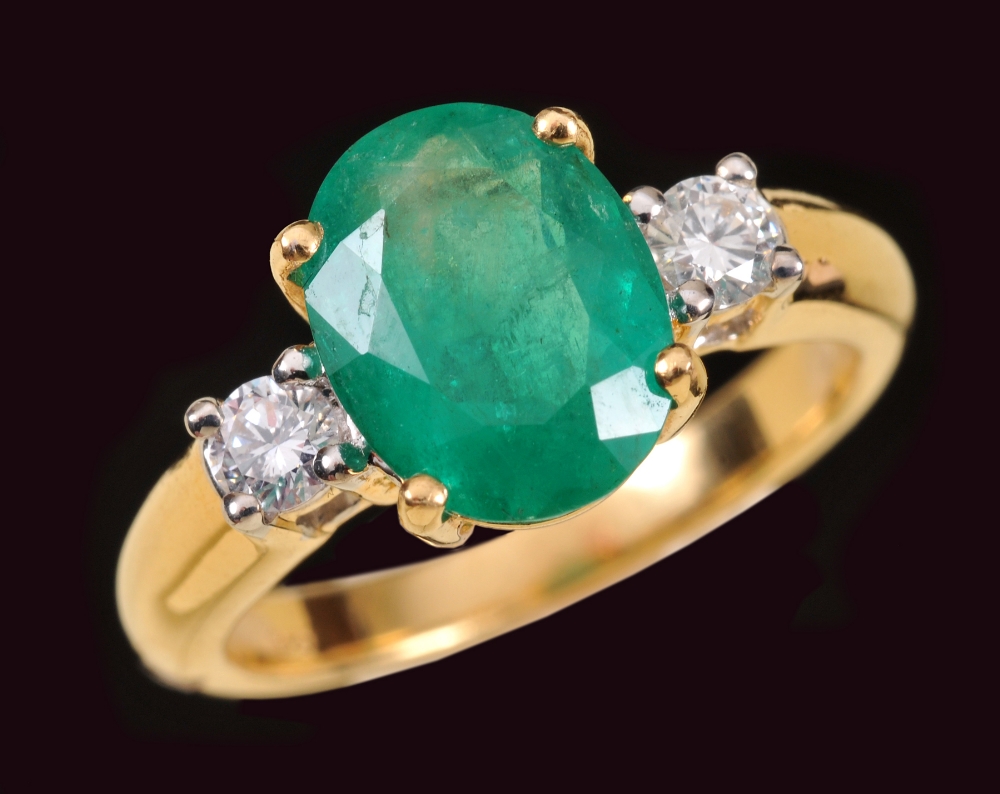 An Emerald and Diamond three stone Ring claw-set oval-cut emerald btween two brilliant-cut