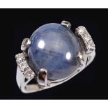 A Star Sapphire and Diamond Ring claw-set blue-grey sapphire cabochon between trios of brilliant-cut