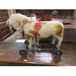 A Steiff plush dappled white Horse with saddle and stirrups on a wheeled iron frame, with a pull