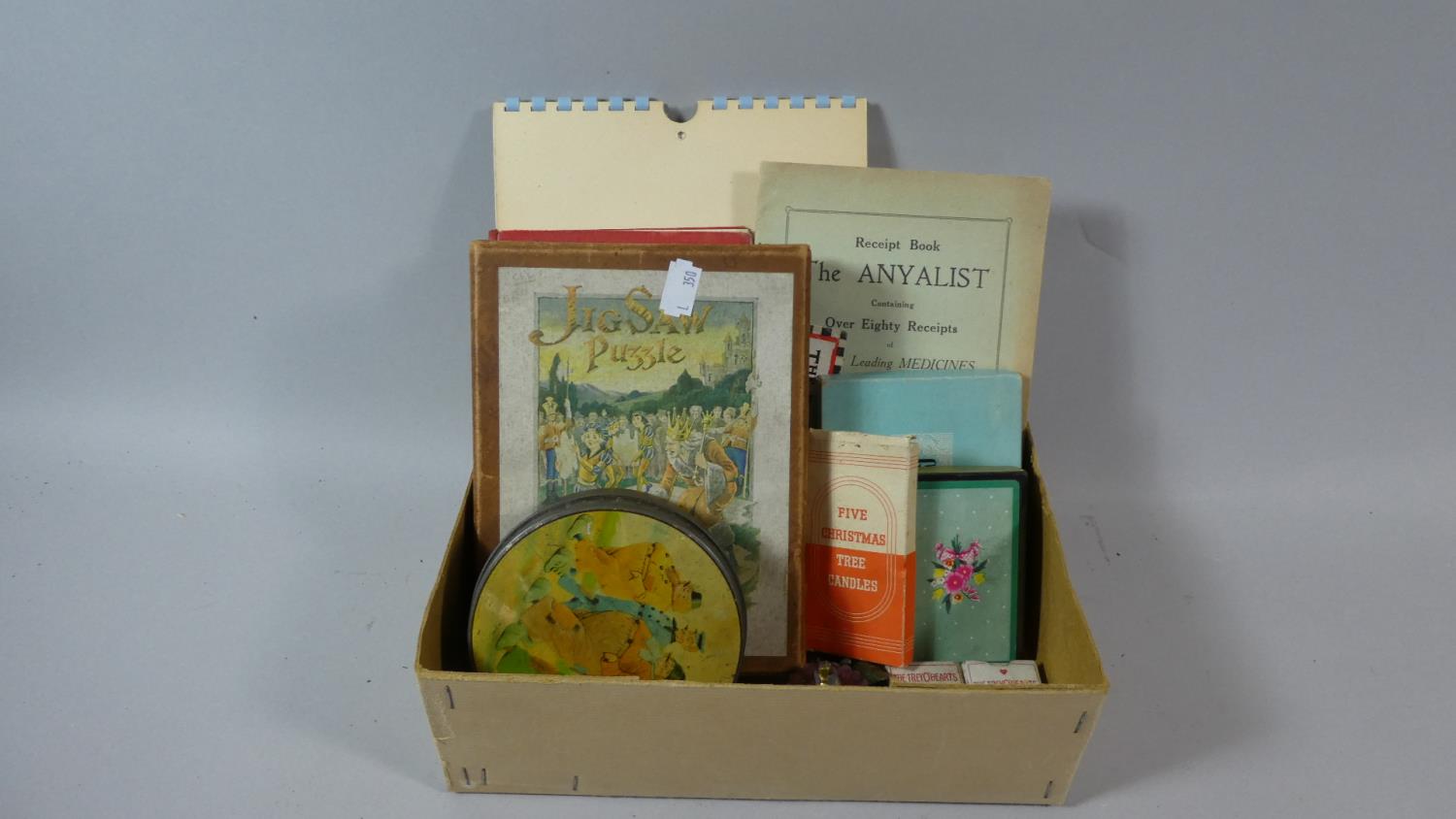 A Box of Printed Ephemera to Include 1950's Risque Calendar, Wooden Jigsaw Puzzle, Vintage Tin,