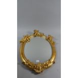 A Gilt Framed Oval Wall Mirror with Cherub Mounts, 53cm High