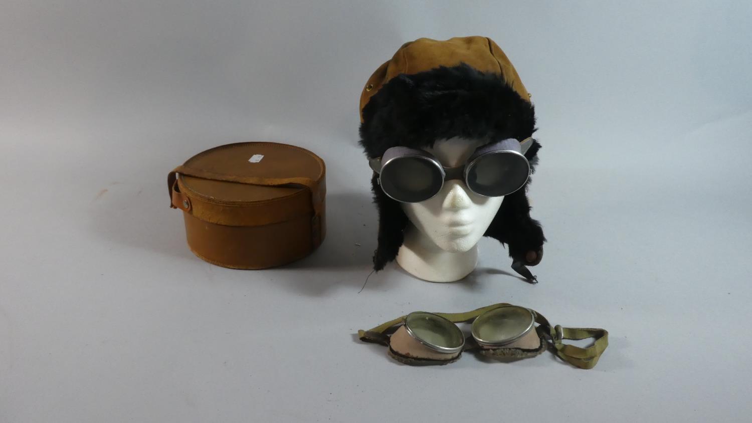 A Circular Leather Collar Box Containing Vintage Driving Goggles and Hat