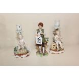 A PAIR OF CONTINENTAL PORCELAIN CANDLESTICKS MARKED R TO THE BASE TOGETHER WITH ANOTHER FIGURE OF