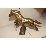 A SOLID BRASS MODEL OF A HORSE JUMPING A WALL, THE HORSE RESTING ON A PIVOT TO PROVIDE MOVEMENT