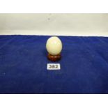 A 19TH CENTURY ELEPHANT IVORY EGG ON WOODEN BASE, 6CM BY 5CM, 154G