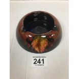 A WILLIAM MOORCROFT FLAMBE ASH TRAY OF CIRCULAR FORM WITH LEAF AND BERRY DECORATION, MARKED TO