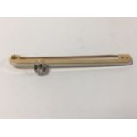 A YELLOW METAL BAR BROOCH WITH SINGLE DIAMOND MOUNTED TO THE TOP, CLAW SET IN WHITE METAL, 5CM WIDE,