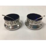 A PAIR OF EDWARDIAN ART NOUVEAU SILVER CIRCULAR SALTS WITH EMBOSSED FLORAL DECORATION WITH BLUE