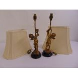 A pair of gilded metal table lamps in the form of putti holding flowers on raised circular bases