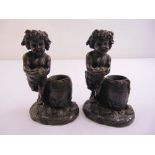 A pair of cast bronze figurines of putti on oval naturalistic bases