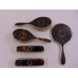 A five piece silver and tortoiseshell dressing table set to include a hand mirror and hair