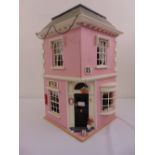 A pink painted corner shop dolls house, the hinged side revealing a quantity of dolls furnishings