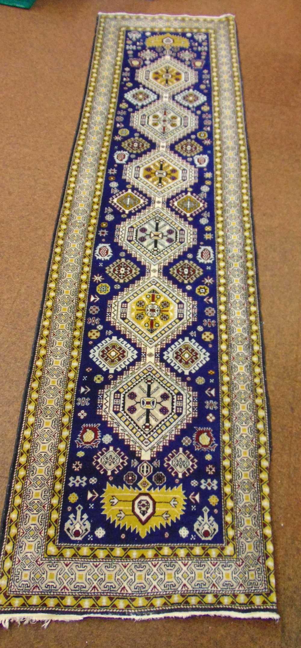 A Persian wool runner, geometric repeating pattern against a dark blue ground, 296 x 78cm