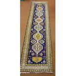 A Persian wool runner, geometric repeating pattern against a dark blue ground, 296 x 78cm