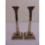 A pair of silver Corinthian column table candlesticks on raised square bases with rosette and swag