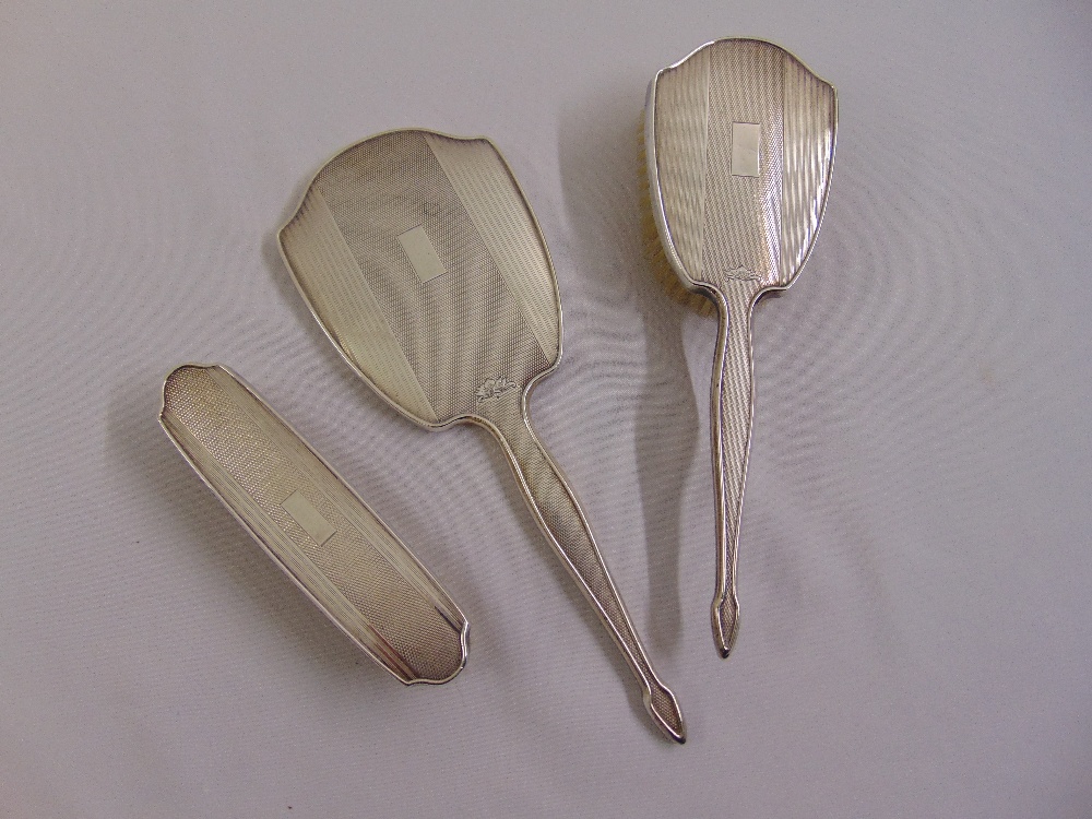 A silver engine turned dressing table hand mirror and two brushes