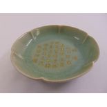 A Chinese celadon dish with scalloped edge and gilded Chinese characters
