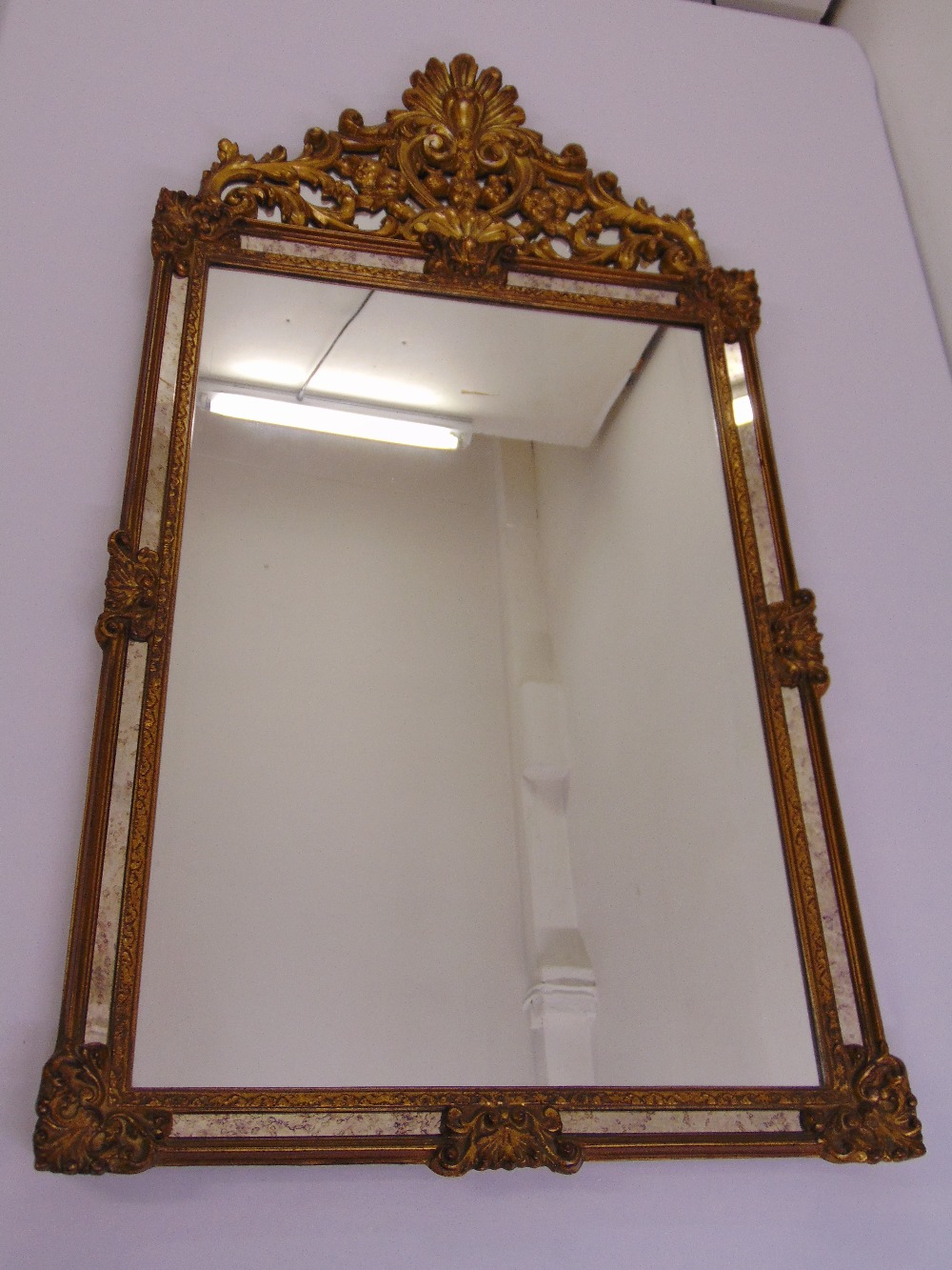 A decorative rectangular gilded wooden wall mirror surmounted by a pierced and carved floral design