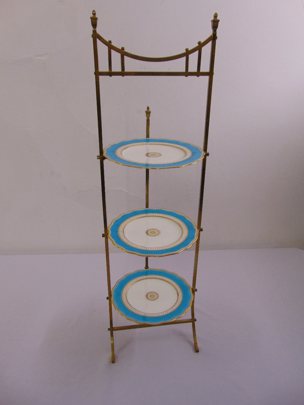 A brass three tier plate stand with three decorative plates