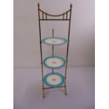 A brass three tier plate stand with three decorative plates