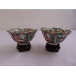 A pair of Chinese famille rose dishes with scalloped edges on hardwood stands