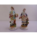 A pair of continental porcelain figurines of a lady and man carrying flowers, on raised circular