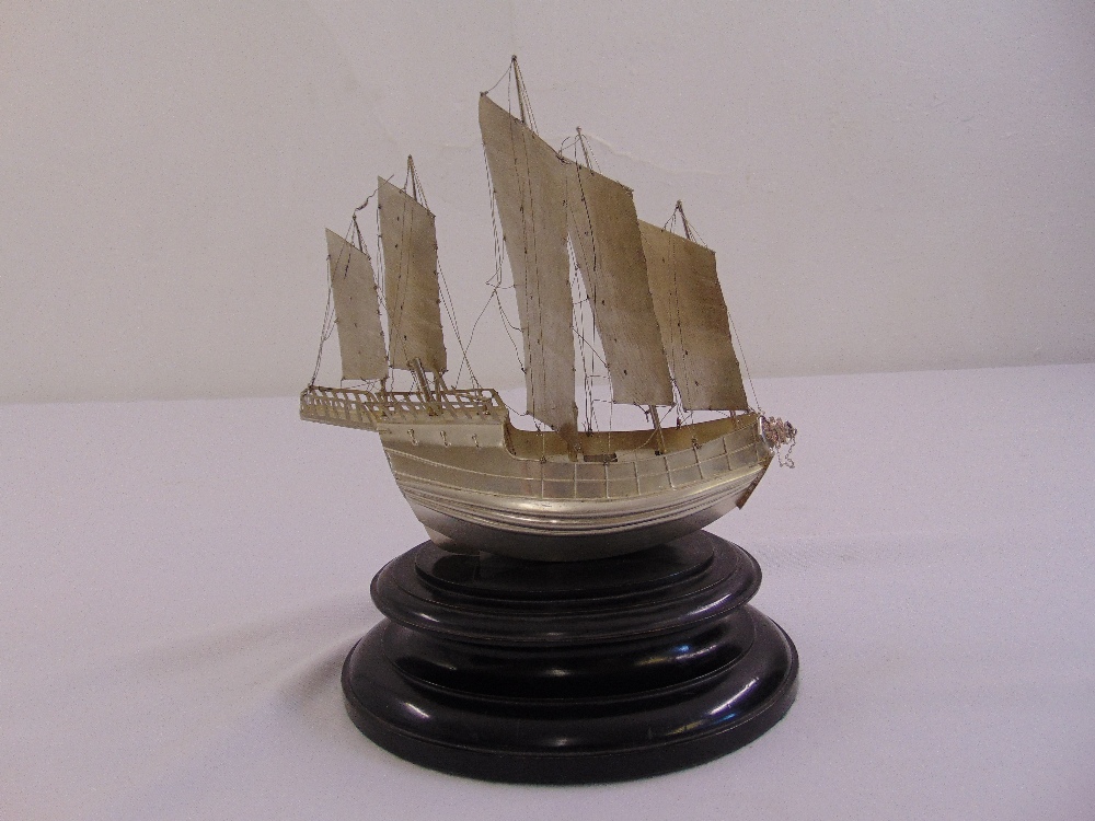 A white metal model of a Chinese Junk mounted on oval hardwood plinth