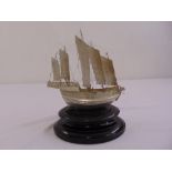 A white metal model of a Chinese Junk mounted on oval hardwood plinth