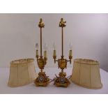 A pair of gilded metal table lamps on raised square bases surmounted by putti finials with silk