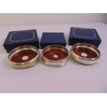 Three silver wine bottle coasters with turned wooden bases all in original packaging