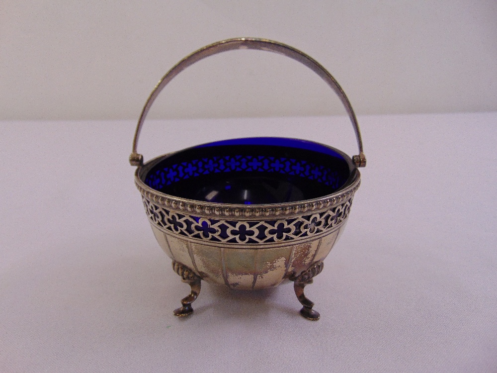 A silver circular bonbon dish with swing handle on four pad feet to include blue glass liner,